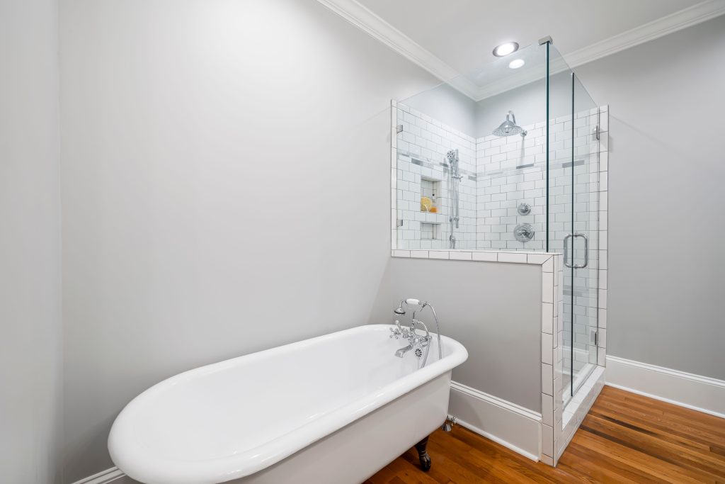 Freestanding clawfoot tub beside a tiled glass shower enclosure